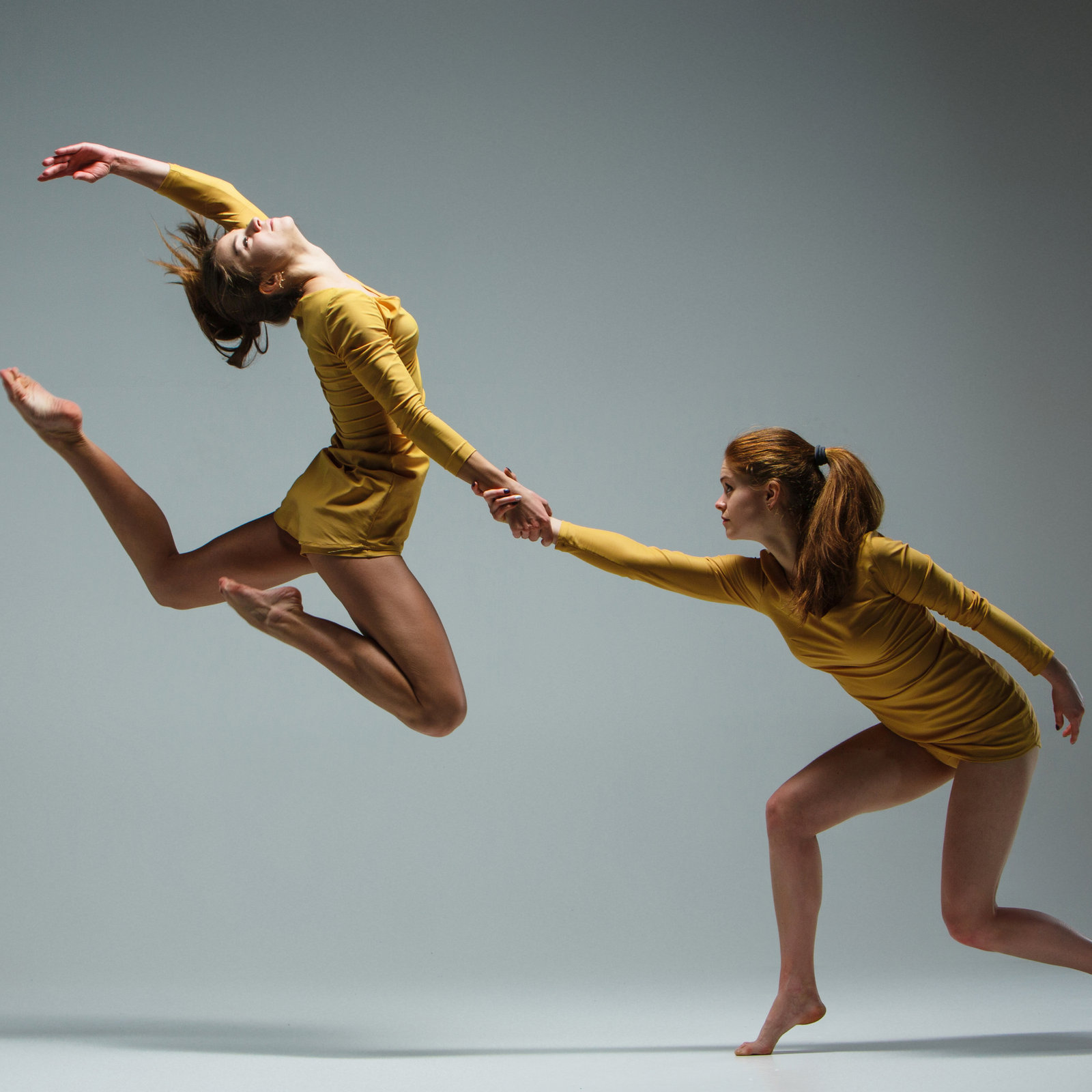 Two modern dancers mid-leap in mustard costumes